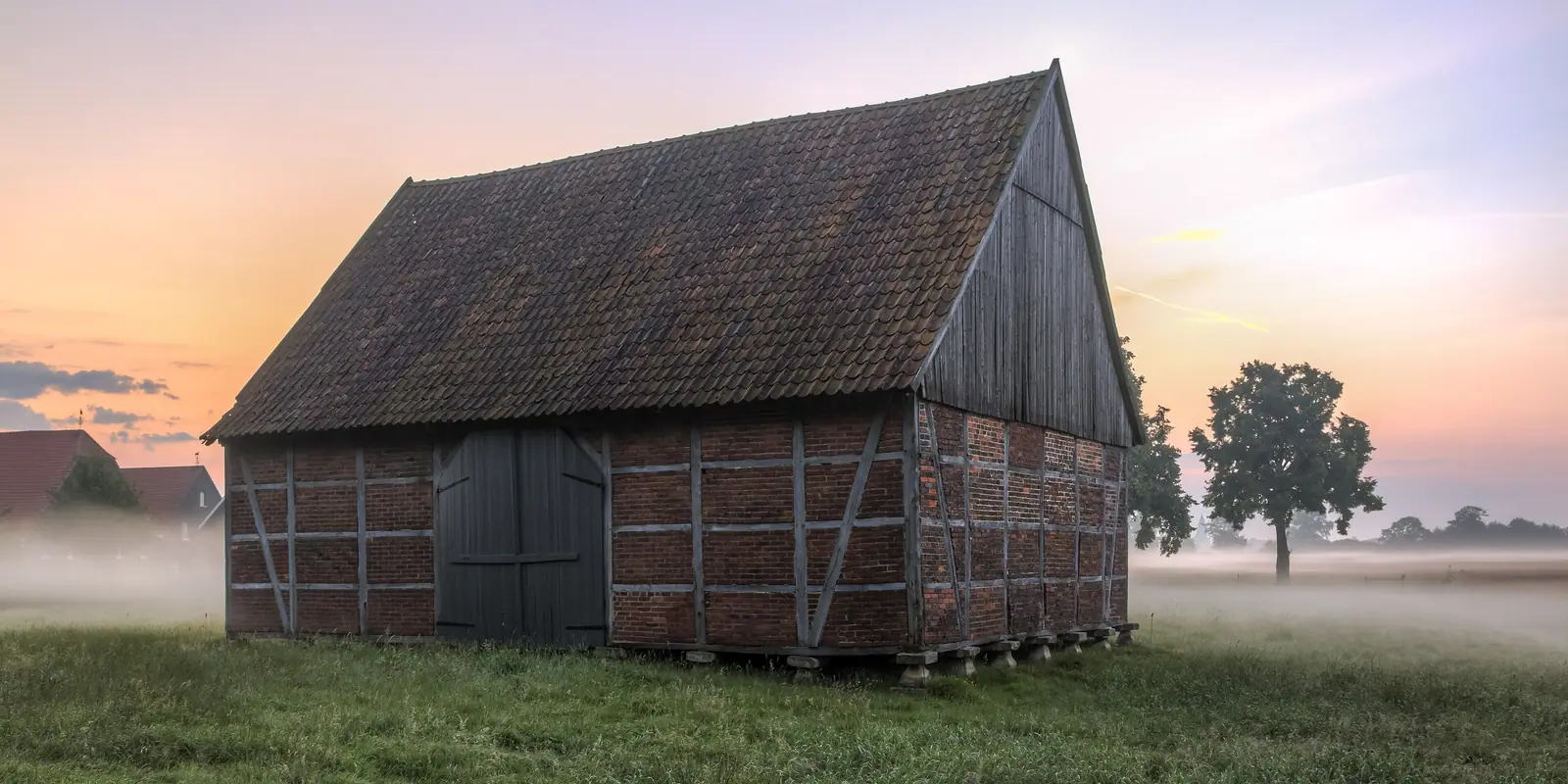 Borda de madera y ladrillo al amanecer, con niebla en el prado
