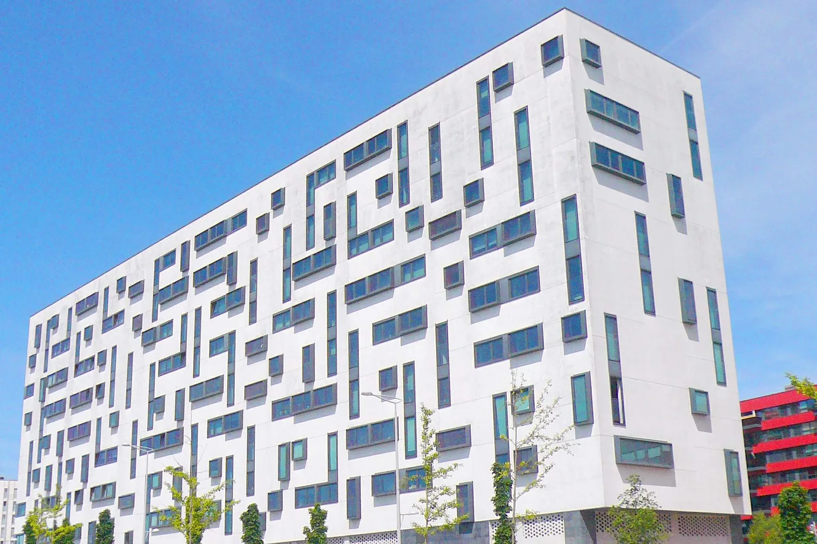 Edificio de viviendas blanco con ventanas de distintos tamaños, contra el cielo azul (foto de ejemplo)