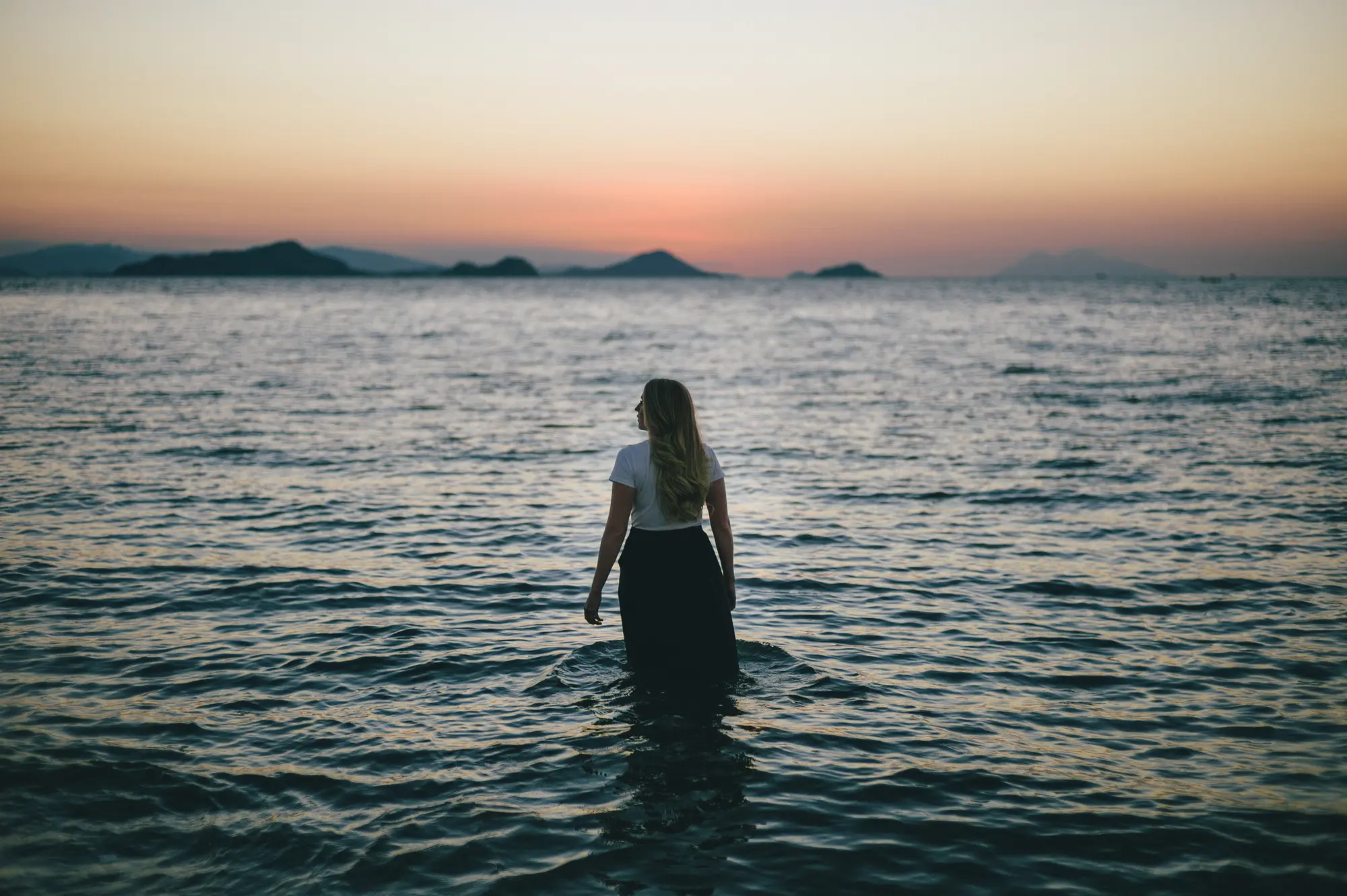 Una mujer de espaldas entra en el mar al atardecer
