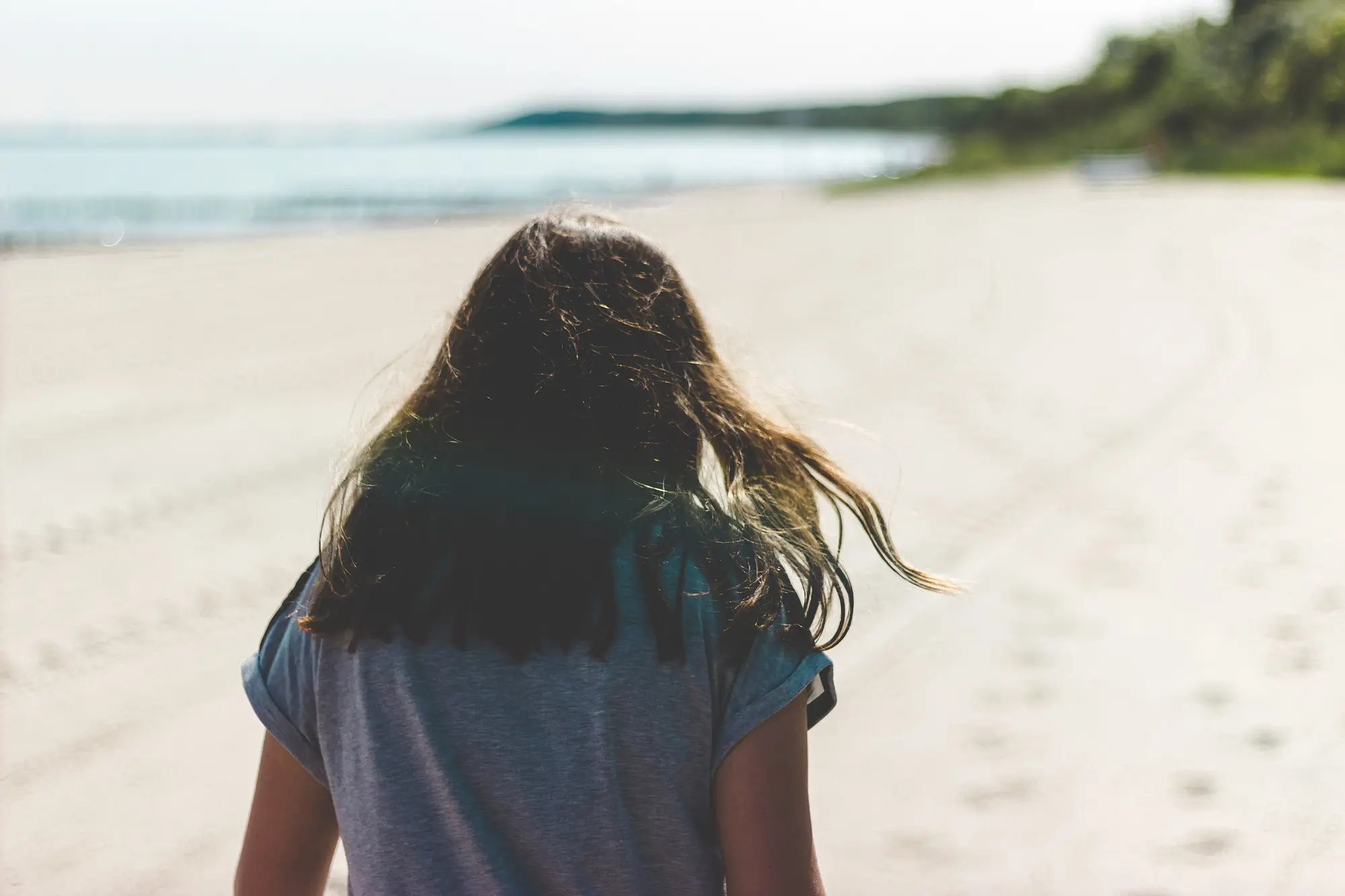 Una chica de espaldas camina por la playa, con el pelo al viento