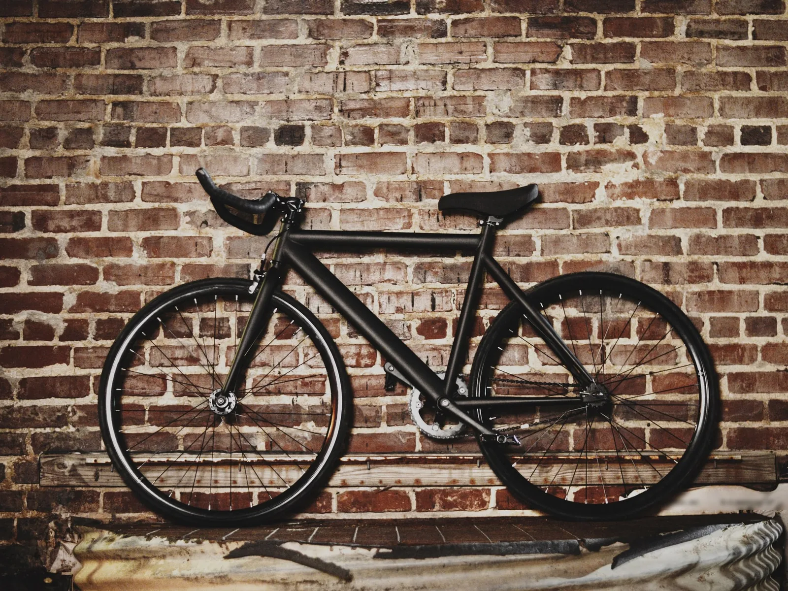 Bici de pista negra, sin marcas, apoyada en un muro de ladrillo viejo